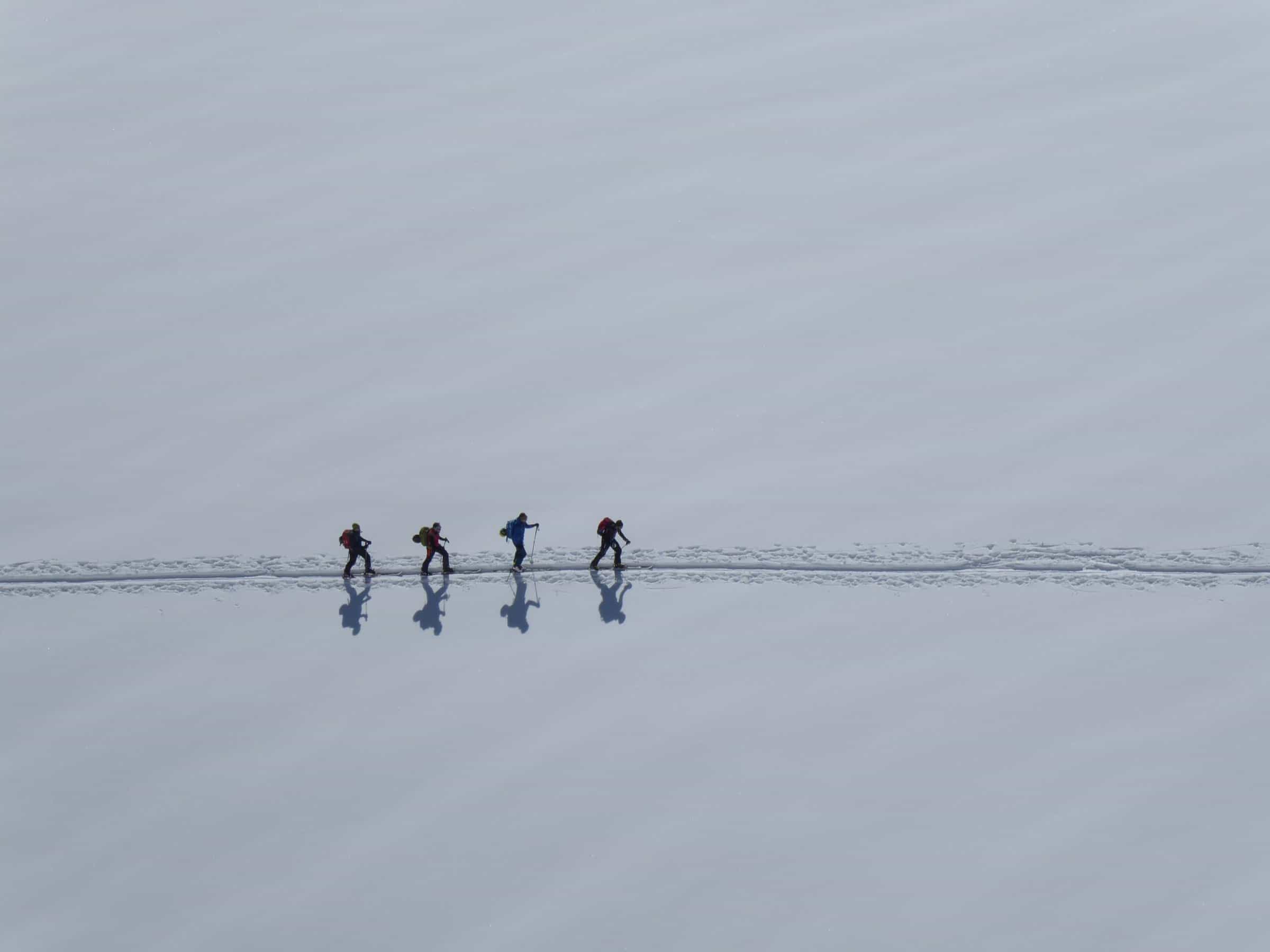 Gruppo di scialpinisti in fila lungo una traccia in piano